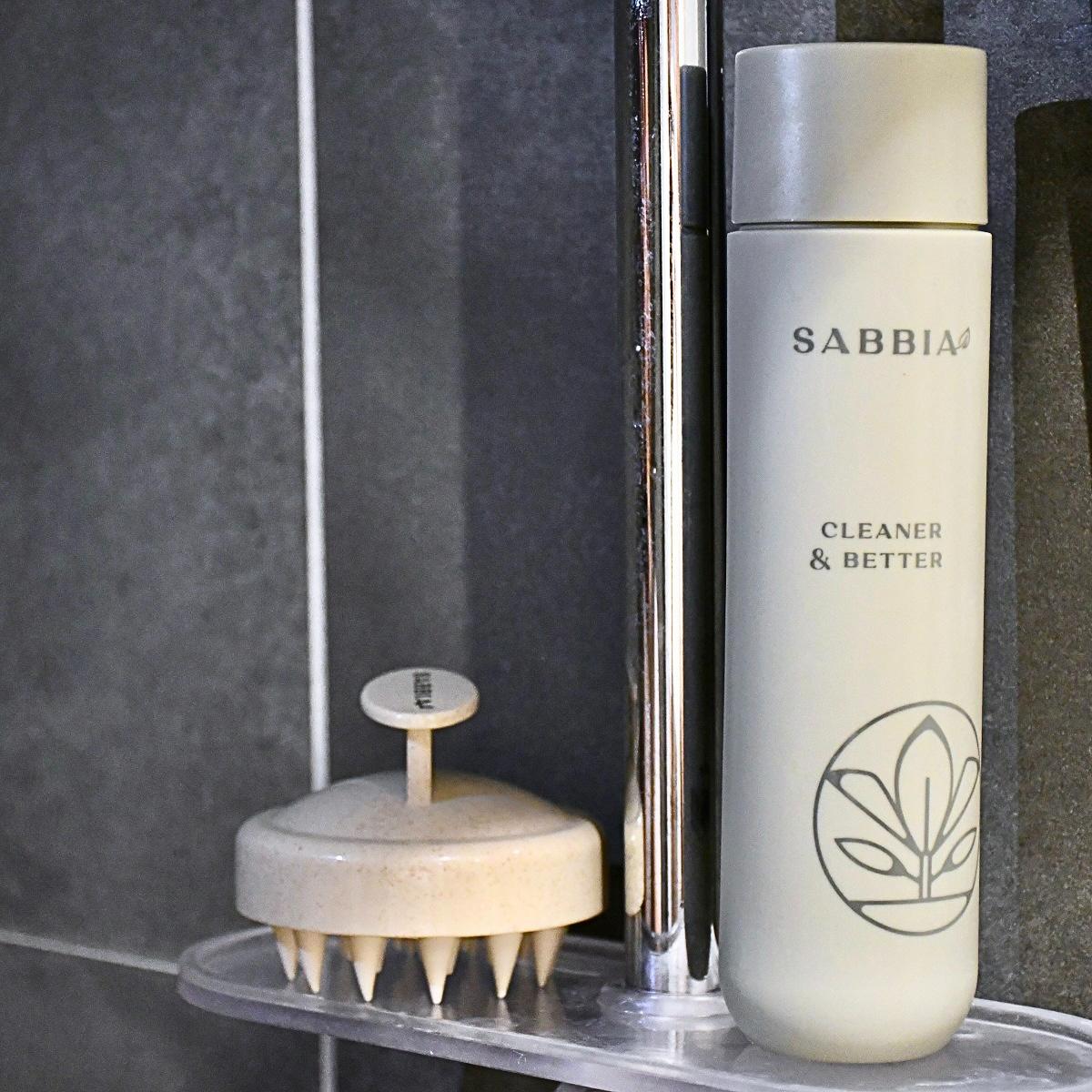 Sabbia šampón a masážna kefka na vlasy uložené na sprchovej poličke v kúpeľni.